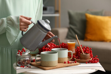 Young woman pouring tasty viburnum tea from teapot into cup at home