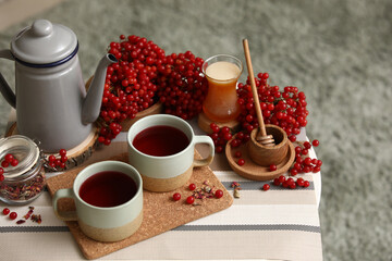 Teapot and cups of tasty viburnum tea on table in interior of living room, closeup