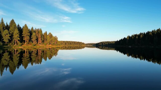 Smooth aerial drone shot flying low over perfectly still lake water reflecting an inverted forest landscape and clear sky perfectly still lake water, serenity, pond
