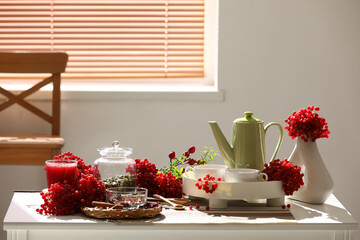 Teapot and cups of hot viburnum tea on table near window in living room