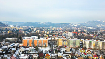 Aerial view of a city in a valley surrounded by snowy mountains with colorful apartment buildings in the foreground during winter