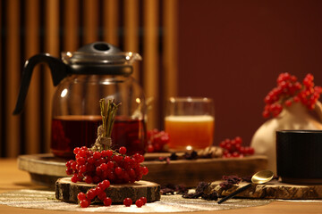Teapot and cup of hot viburnum tea on table near red wall in living room, closeup
