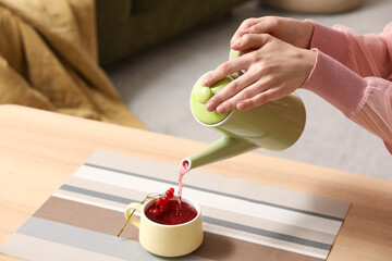 Young woman pouring tasty viburnum tea from teapot into cup at home, closeup