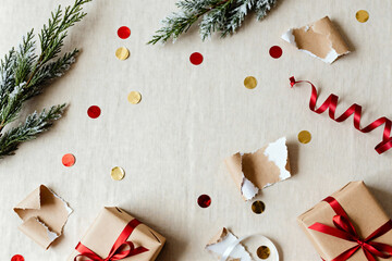Clean minimalist flat lay after Christmas with gold and red confetti, torn wrapping paper, ribbon curls, subtle soft shadows and winter greenery on beige linen