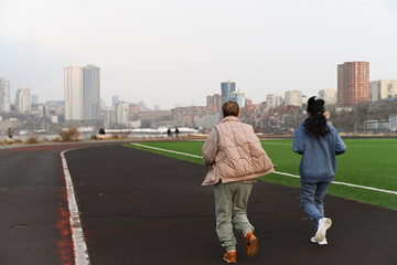 two women friends 50 and 60 years old running at a stadium in the early morning in Vladivostok, back view