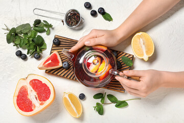 Female hands with teapot of tasty fruit tea and ingredients on white grunge background