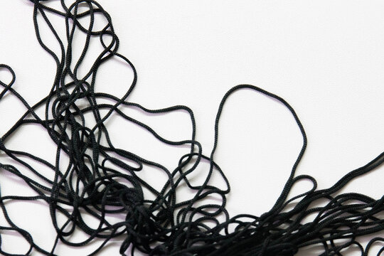 A cluster of thin black cords lies in a loose, chaotic tangle against a clean white background