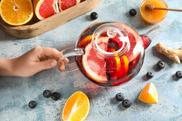 Female hand with glass teapot of hot fruit tea on blue grunge background, closeup