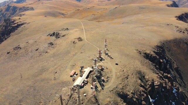 Aerial view of a remote telecommunication relay station featuring multiple towers and buildings situated on a high, barren mountain ridge