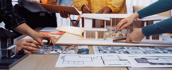 A dynamic architectural design meeting showcases professionals collaborating over blueprints and a model, emphasizing creativity, teamwork, and planning in a modern workspace. SACTR