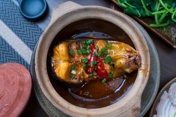Savory clay pot braised fish featuring rich caramel sauce, topped with fresh green onions and spicy red chilies.