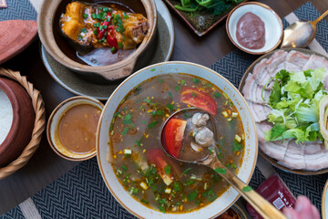 Refreshing sour clam soup with tomatoes and herbs, served alongside braised fish and boiled pork in a traditional Hue meal.