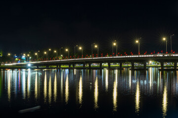 Illuminated bridge in Hue at night featuring starburst streetlights, red flags, and golden reflections on the dark river water.