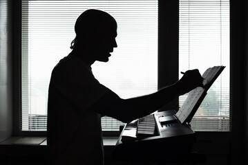 Silhouette of male pianist playing musical instrument at home. Silhouette of a man writing music notes while composing at keyboard
