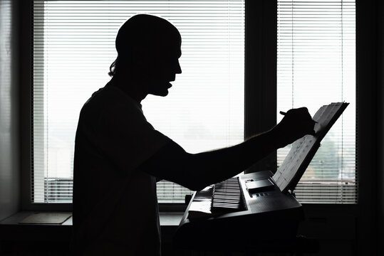 Silhouette of male pianist playing musical instrument at home. Silhouette of a man writing music notes while composing at keyboard