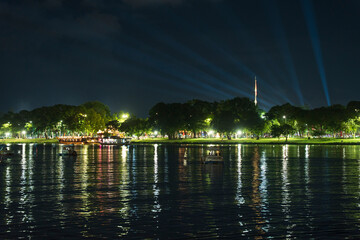 Dramatic green spotlights fan out over the Perfume River at night, illuminating boats and reflecting on the dark water surface.