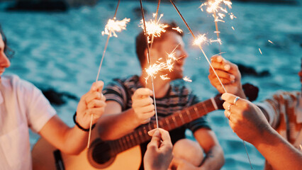 People, hands and night with sparklers on beach for new year, outdoor event or social gathering. Group, friends or fireworks with celebration in late evening for holiday reunion or weekend getaway