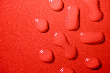 Closeup view of white fluid drops on a textured red background