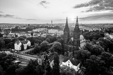 Obraz premium Morning light dances on the iconic Vysehrad Basilica of St. Peter and St. Paul. The historic site stands majestically against the backdrop of Prague's skyline, surrounded by lush greenery.