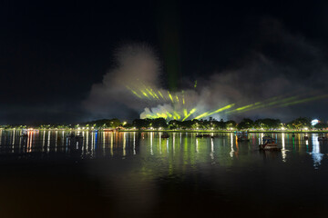Dramatic green spotlights fan out over the Perfume River at night, illuminating boats and reflecting on the dark water surface.