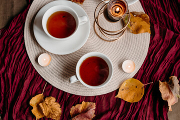 Black tea served in white cups on a deep burgundy tablecloth, with soft candlelight and a piece of cake adding a cozy homelike feel.