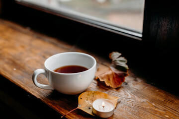 Tea cup by a rainy window with candlelight adding warm soft tones to a calm wooden setup.