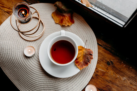 Black tea on a wooden windowsill with raindrops on glass and a burning candle creating a calm rainy-day mood.