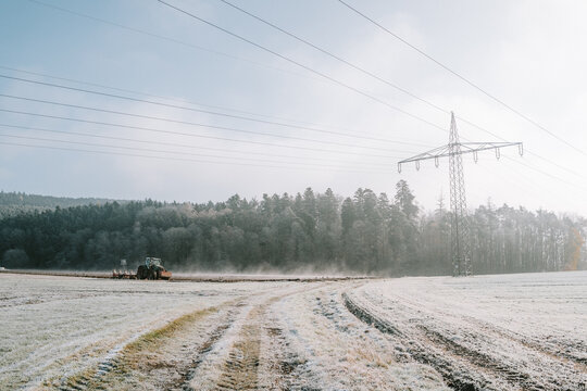 Ein Traktor pfl&uuml;gt einen dampfenden Acker an einem kalten Wintermorgen mit Sonnenschein