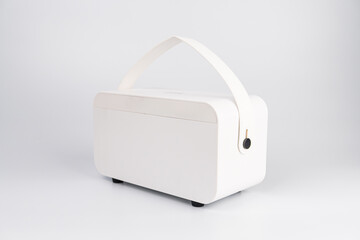 Modern mini guitar amp speaker on light gray, positioned next to a white microwave Rectangular shape with rounded top edge and two control buttons Brand logo in black text Studio setting with even