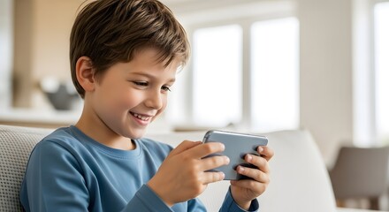 Caucasian kid boy with cute smile sitting on coach and playing video game on smartphone at home. Online mobile entertainment for a child, video call