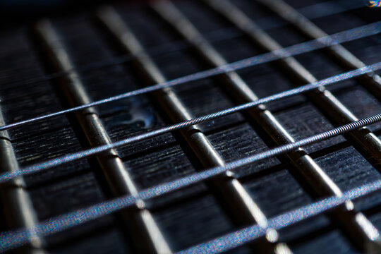 Close-up view of a modern heavy rock electric guitar fretboard, gleaming metallic strings and frets under soft lighting, stage-like background suggesting live performance, muted colors, angled perspe