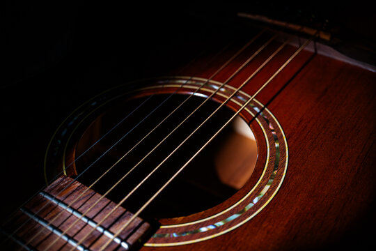 Close-up view of a brown acoustic guitar with steel strings and metal frets, showcasing wood texture and glossy finish The guitar is angled, emphasizing the neck curvature and string alignment Soft