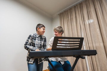 Mother teaching son to play electronic keyboard at home, both smiling and sharing a happy family bonding experience