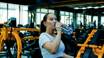The woman is drinking water from a bottle in a gym setting