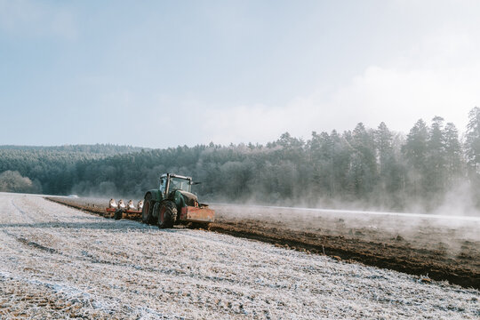 Ein Traktor pfl&uuml;gt einen dampfenden Acker an einem kalten Wintermorgen mit Sonnenschein