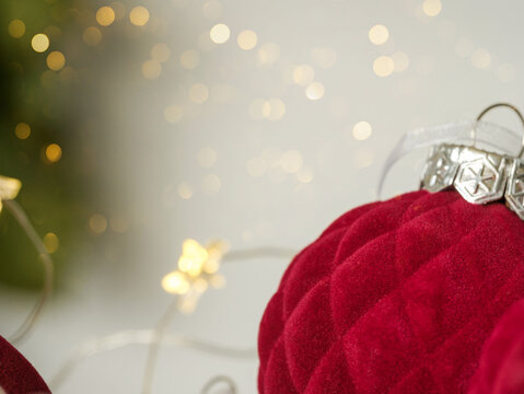 Background for personalized Christmas card. Closeup red burgundy maroon velvet ornaments, blurry gold bokeh, evergreen spruce pine greenery branches, festive twinkle fairy lights.