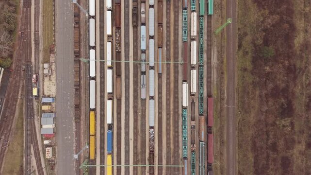 A straight-down aerial view of a busy freight railway yard filled with cargo wagons arranged on multiple parallel tracks. Drone follow a leaving train.