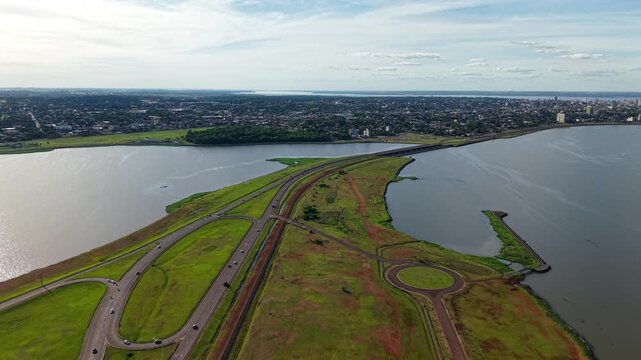 Forward aerial towards Posadas city via east road, with the Paran&aacute; River on the right, a river arm and bridge to the left, and lush vegetation including the botanical garden.