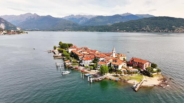 Isola Bella, a picturesque island village on Lake Maggiore, Stresa, showcases charming architecture, docks, and boats, surrounded by the western Alps landscape of northern Italy, Piedmont, drone orbit