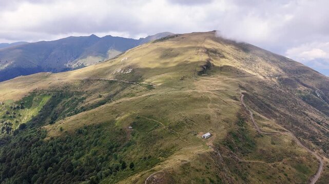 High-angle aerial shot of Cima Monte Grona summit in Lombardy Prealps with Hiking trails wind up grassy slopes towards the peak, offering views of surrounding mountains and landscape near Lake Como.