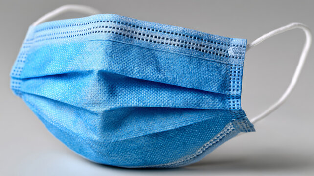 Blue surgical face mask on grey background.