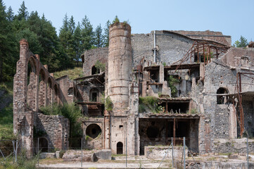 Close-up of the historical ruins of an abandoned cement factory in Castellar de n'Hug, featuring a prominent chimney, arched walls, and severe industrial decay.