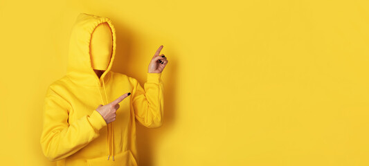 Anonymous faceless figure wearing a yellow hoodie pointing at blank yellow background, ideal for advertising, promotions, and creative concepts.