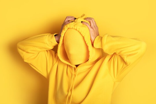 Anonymous individual in a yellow hoodie blends into a seamless yellow background, creating a striking and modern conceptual image.