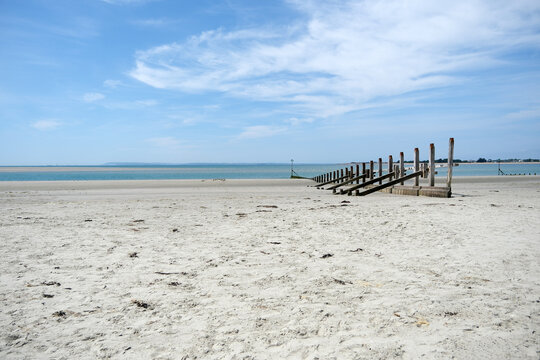 Wooden Sea Defence Structure on Wide Sandy Beach Under Blue Sky
