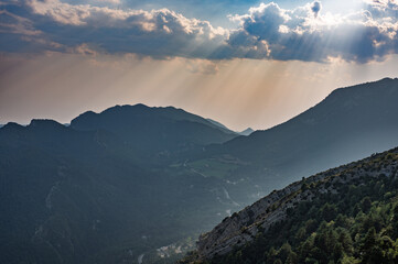 Dramatic sunset landscape over the mountains of Berga, Catalonia, Spain, featuring intense crepuscular sun rays piercing through clouds and highlighting the valley below.