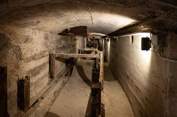 Long exposure view of a dark, abandoned cement factory tunnel showing the rusted metal framework of a defunct conveyor belt system.
