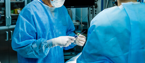 A surgeon wearing sterile gloves holds a large syringe containing medication. A syringe with a needle for intravenous drug administration.