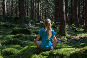 Beautiful relaxed blond woman practicing yoga and meditation in middle of forest. 