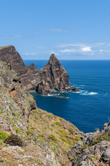 Sheer sea stacks at Ponta de Sao Lourenco Madeira tower over the ocean, bright midday light reveals rugged rock layers and turquoise surf churning below